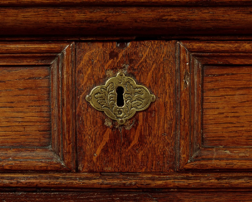 A Charles II solid oak chest of drawers featuring geometric panelled drawer fronts and brass teardrop handles. View VII