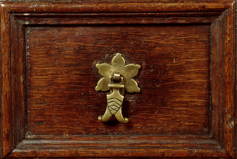 A Charles II solid oak chest of drawers featuring geometric panelled drawer fronts and brass teardrop handles. View VIII