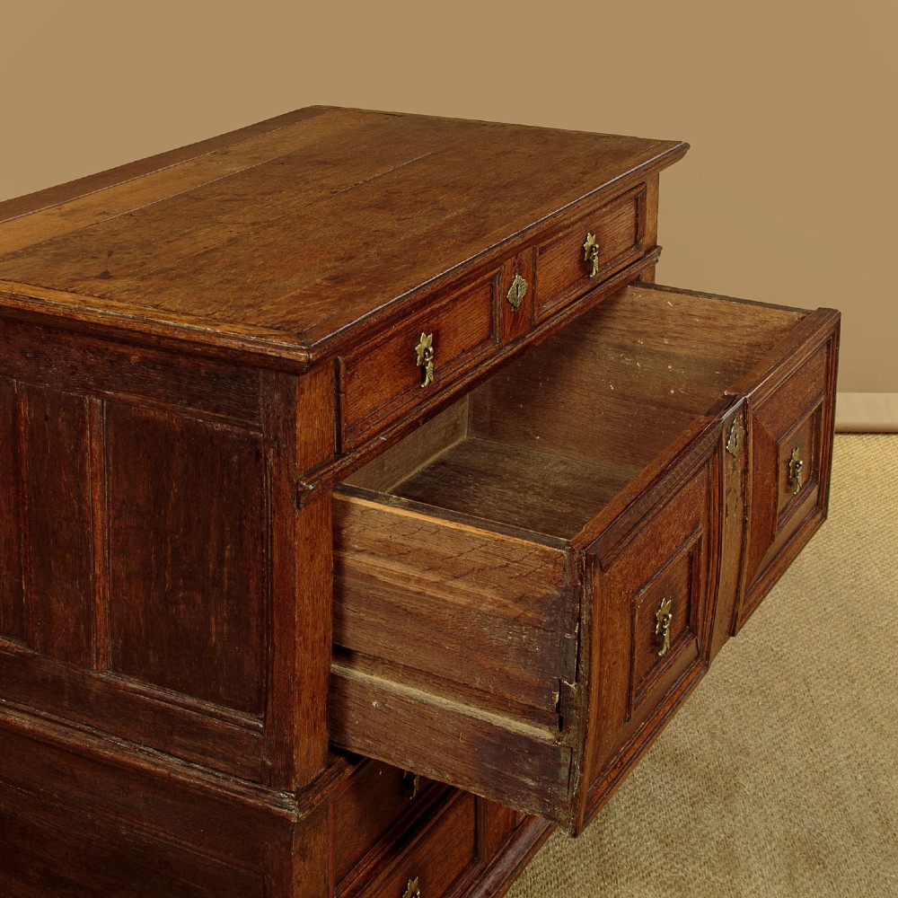 A Charles II solid oak chest of drawers featuring geometric panelled drawer fronts and brass teardrop handles. View IX
