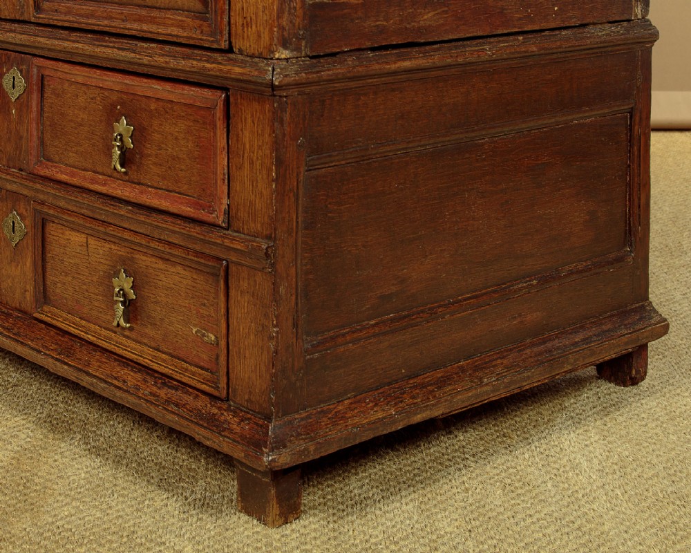 A Charles II solid oak chest of drawers featuring geometric panelled drawer fronts and brass teardrop handles. View X