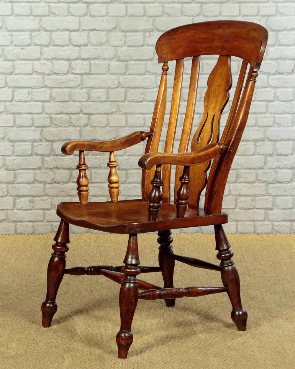 A Victorian highback wooden armchair featuring turned legs, curved armrests, a contoured seat, and a pierced back splat.