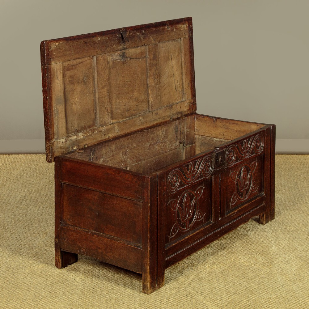 A dark oak coffer from circa 1700 featuring carved panel fronts with floral motifs and a hinged wooden top. View V