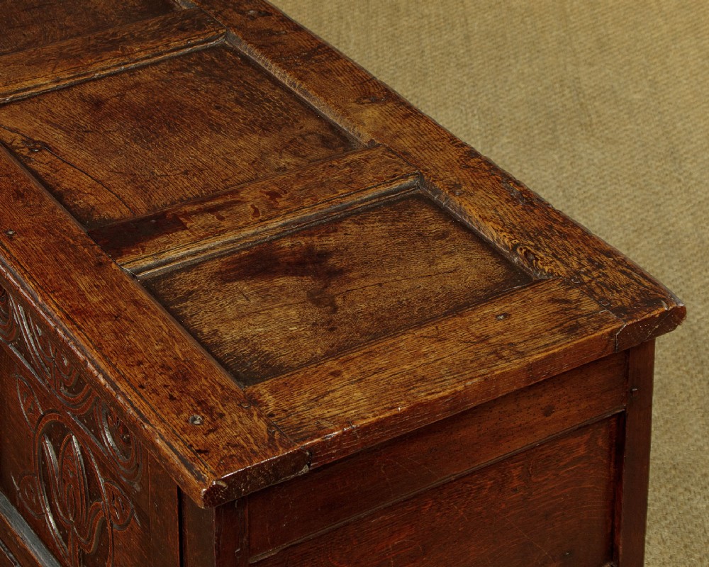 A dark oak coffer from circa 1700 featuring carved panel fronts with floral motifs and a hinged wooden top. View VII