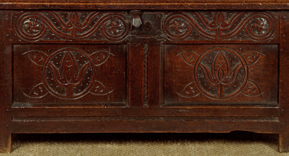 A dark oak coffer from circa 1700 featuring carved panel fronts with floral motifs and a hinged wooden top. View IX