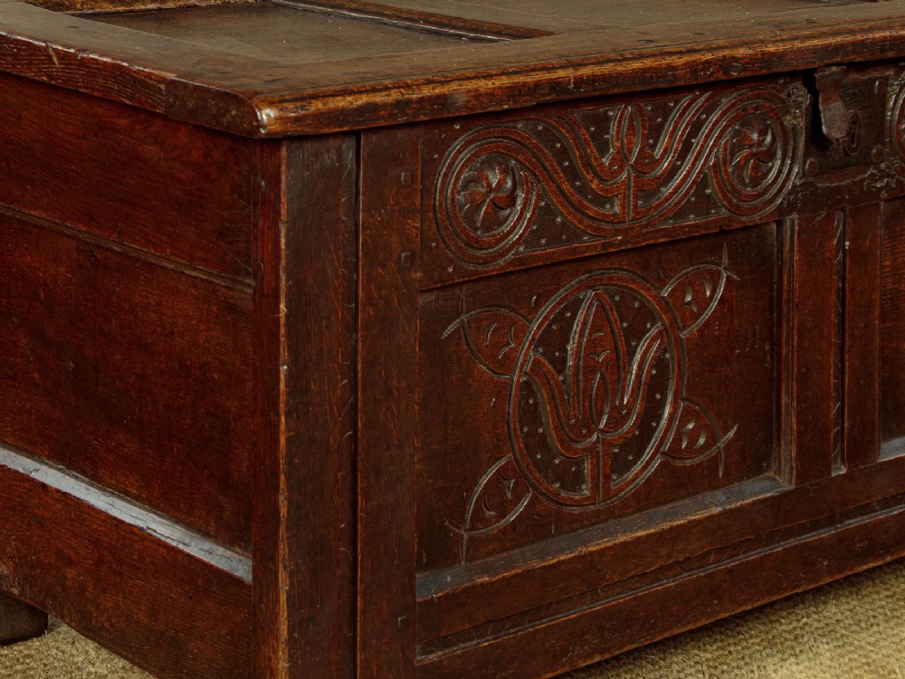 A dark oak coffer from circa 1700 featuring carved panel fronts with floral motifs and a hinged wooden top. View X