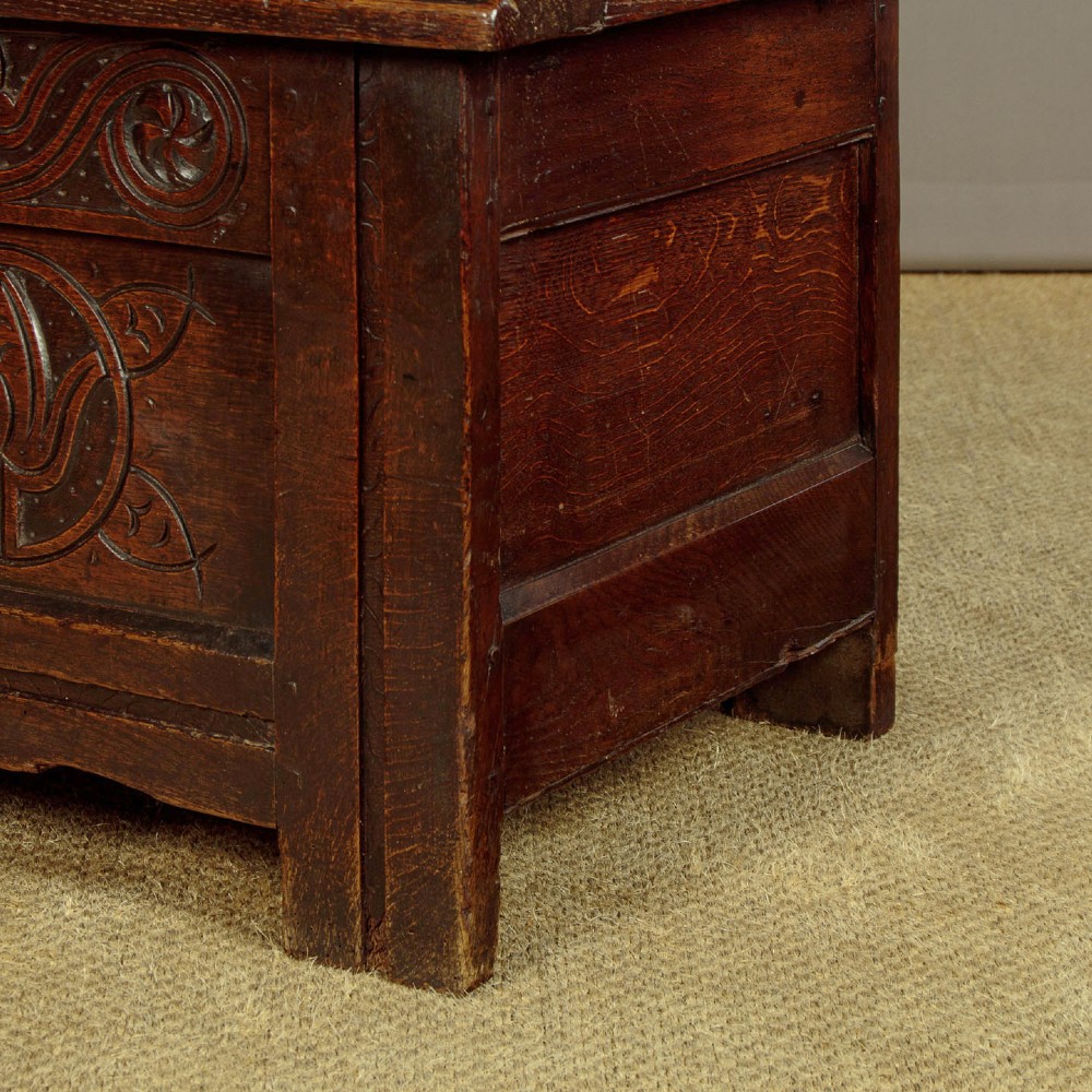 A dark oak coffer from circa 1700 featuring carved panel fronts with floral motifs and a hinged wooden top. View XII
