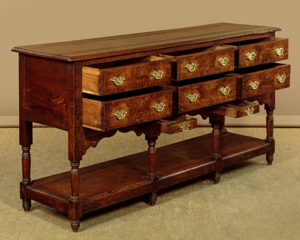 A Georgian oak Welsh dresser base featuring eight drawers with brass handles, a scalloped apron, turned front legs, and an open potboard lower shelf. View V