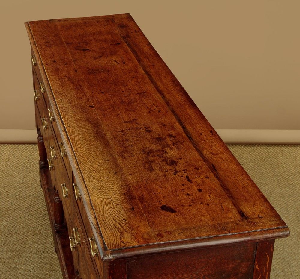 A Georgian oak Welsh dresser base featuring eight drawers with brass handles, a scalloped apron, turned front legs, and an open potboard lower shelf. View VI