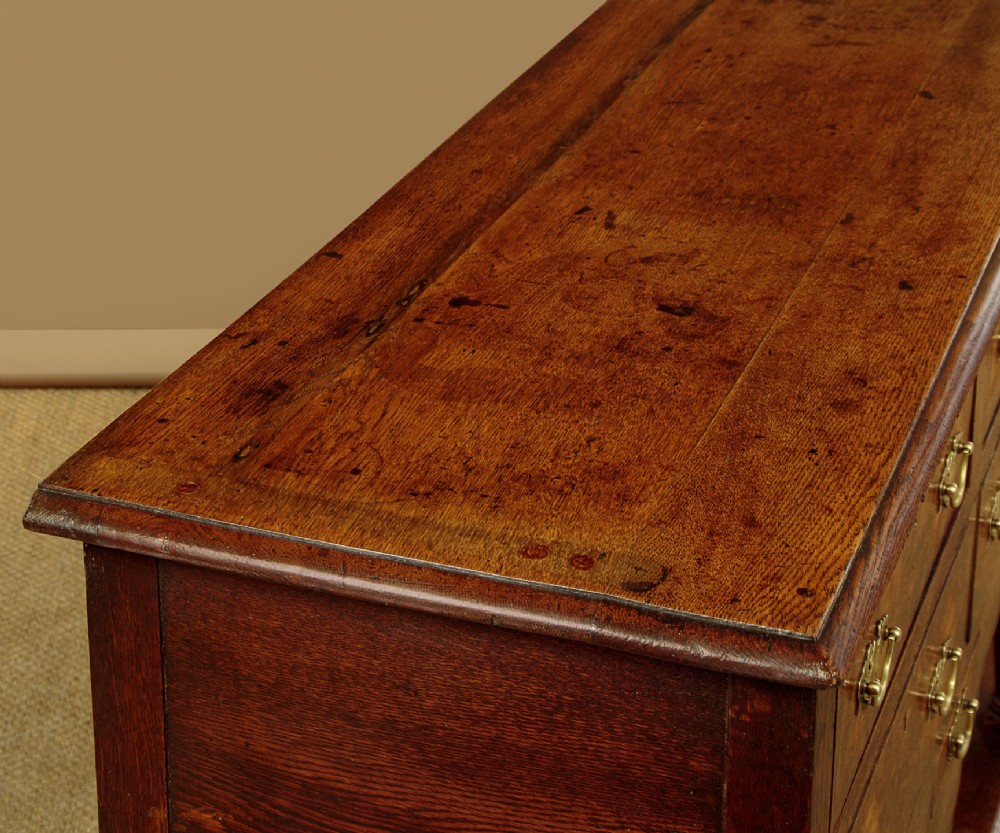A Georgian oak Welsh dresser base featuring eight drawers with brass handles, a scalloped apron, turned front legs, and an open potboard lower shelf. View VII