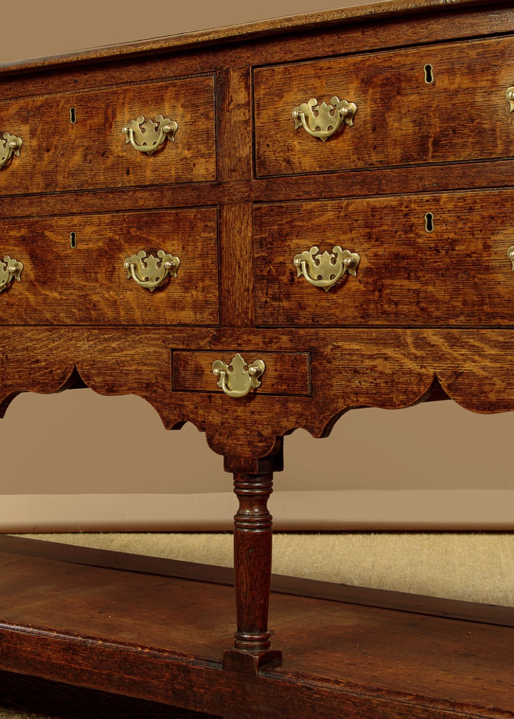 A Georgian oak Welsh dresser base featuring eight drawers with brass handles, a scalloped apron, turned front legs, and an open potboard lower shelf. View VIII