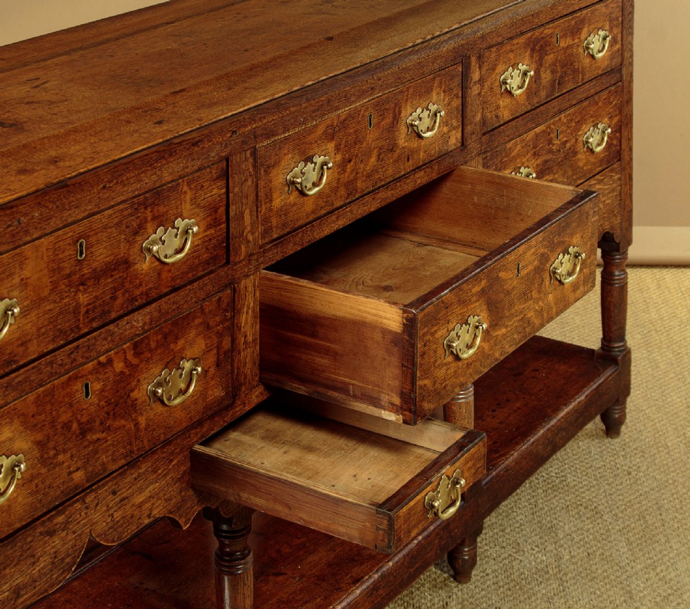 A Georgian oak Welsh dresser base featuring eight drawers with brass handles, a scalloped apron, turned front legs, and an open potboard lower shelf. View XI
