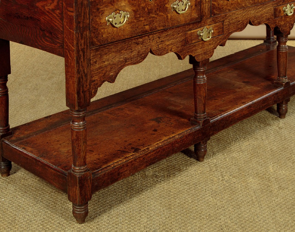 A Georgian oak Welsh dresser base featuring eight drawers with brass handles, a scalloped apron, turned front legs, and an open potboard lower shelf. View XII