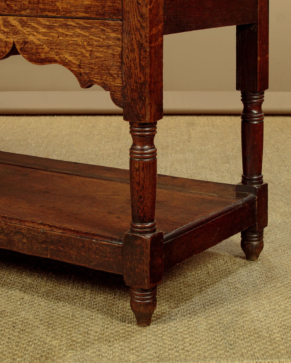 A Georgian oak Welsh dresser base featuring eight drawers with brass handles, a scalloped apron, turned front legs, and an open potboard lower shelf. View XIII