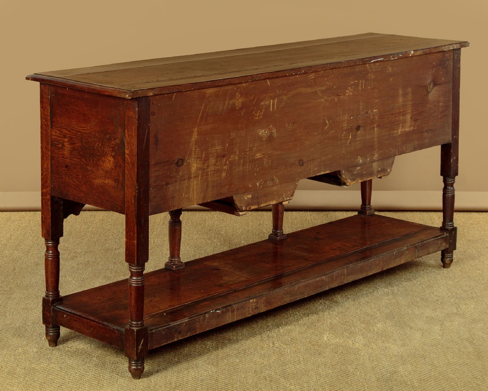 A Georgian oak Welsh dresser base featuring eight drawers with brass handles, a scalloped apron, turned front legs, and an open potboard lower shelf. View XIV