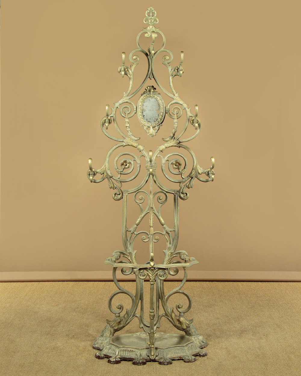An ornate Victorian painted cast iron hall stand featuring scrollwork motifs, multiple coat hooks, a central oval mirror, and an umbrella drip tray base.