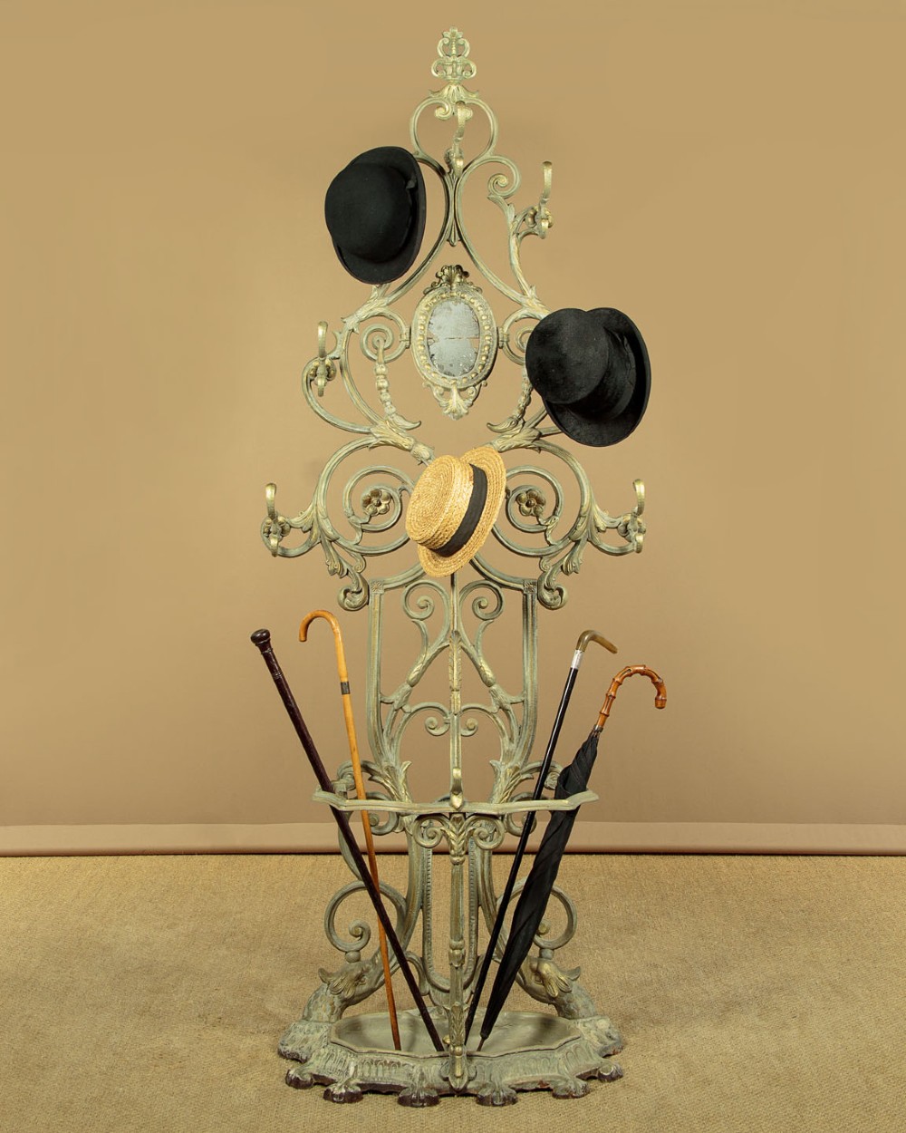An ornate Victorian painted cast iron hall stand featuring scrollwork motifs, multiple coat hooks, a central oval mirror, and an umbrella drip tray base. View II