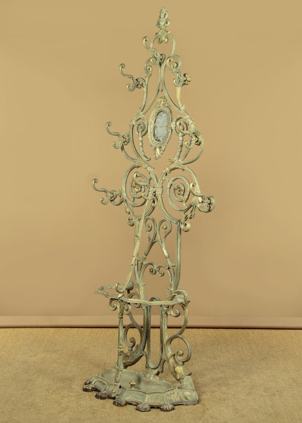 An ornate Victorian painted cast iron hall stand featuring scrollwork motifs, multiple coat hooks, a central oval mirror, and an umbrella drip tray base. View IV