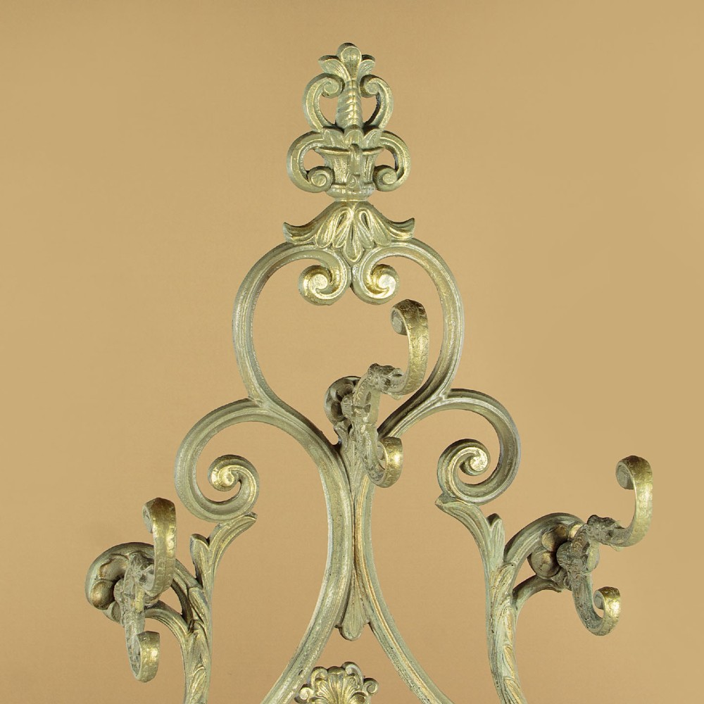 An ornate Victorian painted cast iron hall stand featuring scrollwork motifs, multiple coat hooks, a central oval mirror, and an umbrella drip tray base. View V