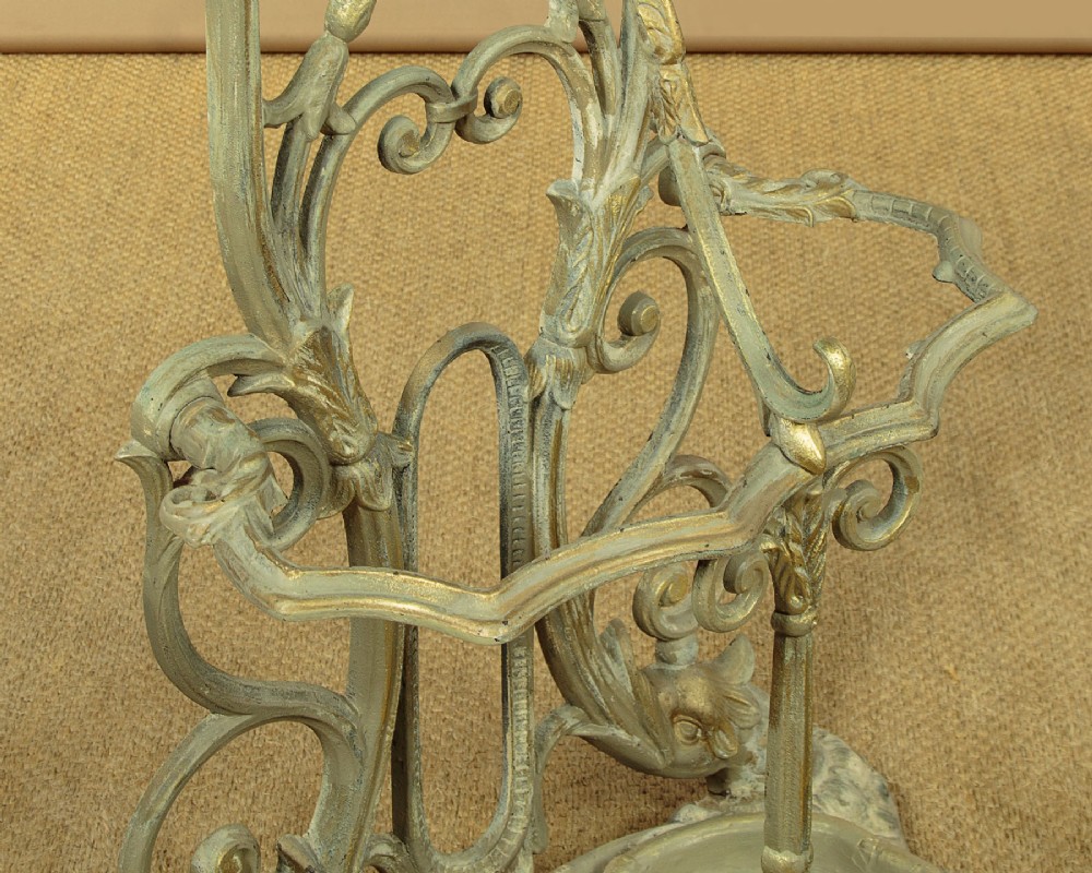 An ornate Victorian painted cast iron hall stand featuring scrollwork motifs, multiple coat hooks, a central oval mirror, and an umbrella drip tray base. View X