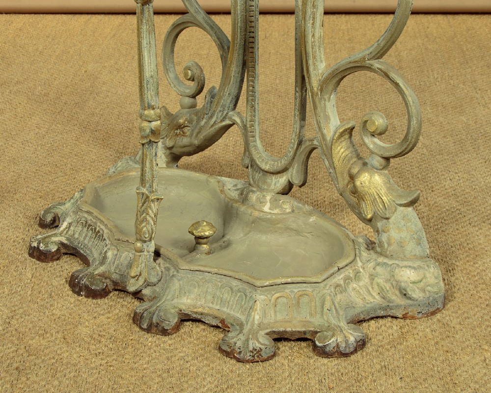 An ornate Victorian painted cast iron hall stand featuring scrollwork motifs, multiple coat hooks, a central oval mirror, and an umbrella drip tray base. View XI