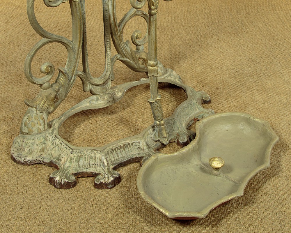 An ornate Victorian painted cast iron hall stand featuring scrollwork motifs, multiple coat hooks, a central oval mirror, and an umbrella drip tray base. View XII