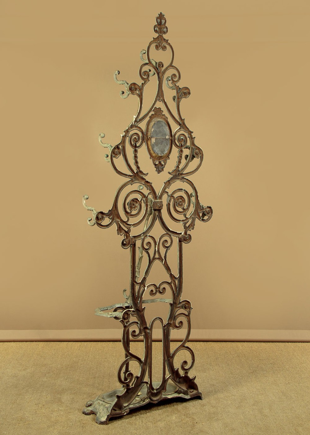 An ornate Victorian painted cast iron hall stand featuring scrollwork motifs, multiple coat hooks, a central oval mirror, and an umbrella drip tray base. View XIII
