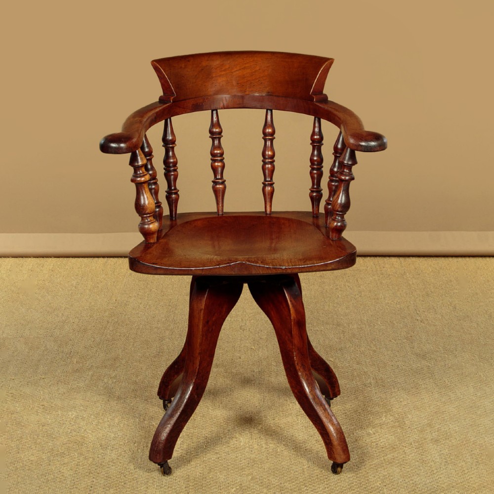 A late Victorian walnut revolving desk chair featuring turned spindles, a curved backrest, a shaped contoured seat, and splayed legs with brass castors.