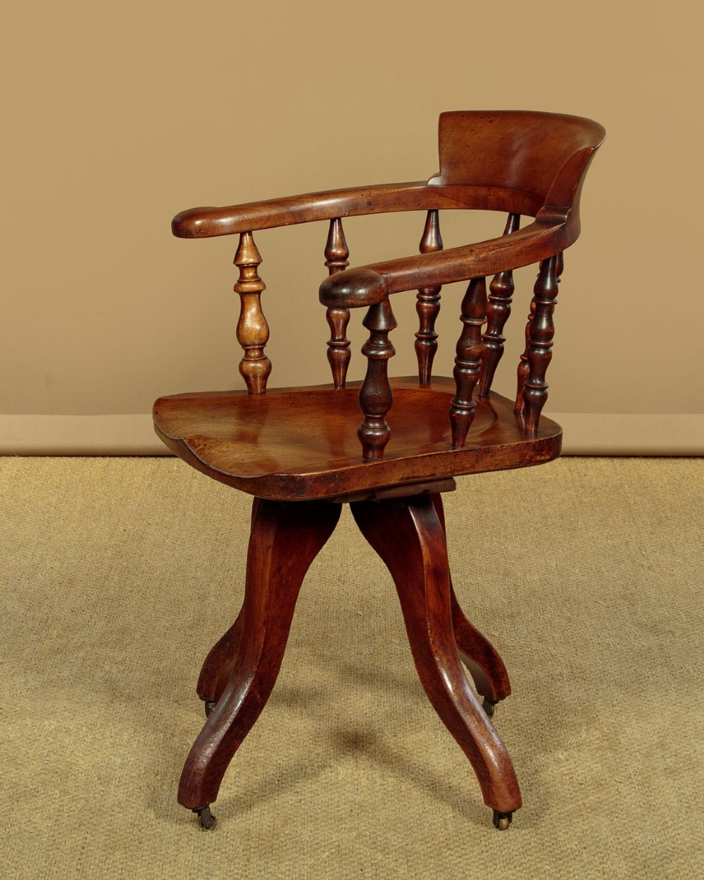 A late Victorian walnut revolving desk chair featuring turned spindles, a curved backrest, a shaped contoured seat, and splayed legs with brass castors. View II