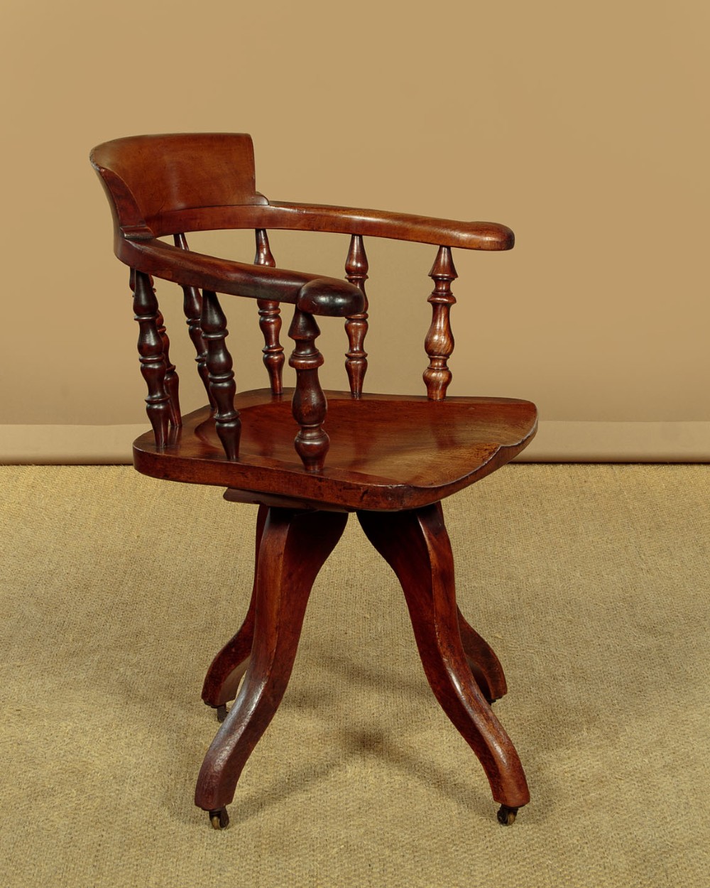 A late Victorian walnut revolving desk chair featuring turned spindles, a curved backrest, a shaped contoured seat, and splayed legs with brass castors. View III