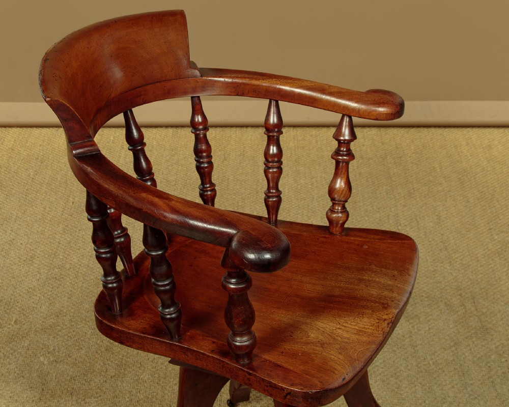 A late Victorian walnut revolving desk chair featuring turned spindles, a curved backrest, a shaped contoured seat, and splayed legs with brass castors. View IV