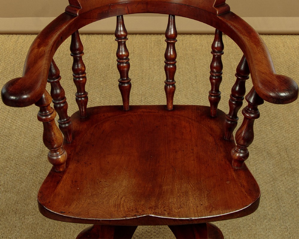 A late Victorian walnut revolving desk chair featuring turned spindles, a curved backrest, a shaped contoured seat, and splayed legs with brass castors. View V