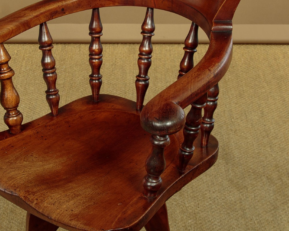 A late Victorian walnut revolving desk chair featuring turned spindles, a curved backrest, a shaped contoured seat, and splayed legs with brass castors. View VI