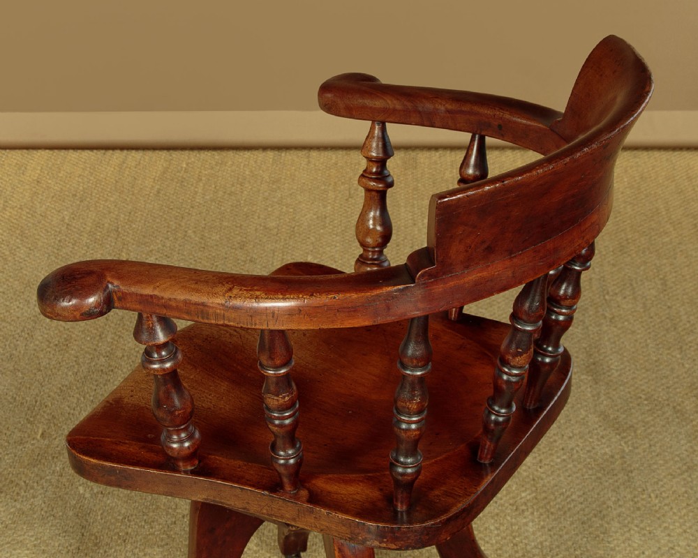 A late Victorian walnut revolving desk chair featuring turned spindles, a curved backrest, a shaped contoured seat, and splayed legs with brass castors. View VII