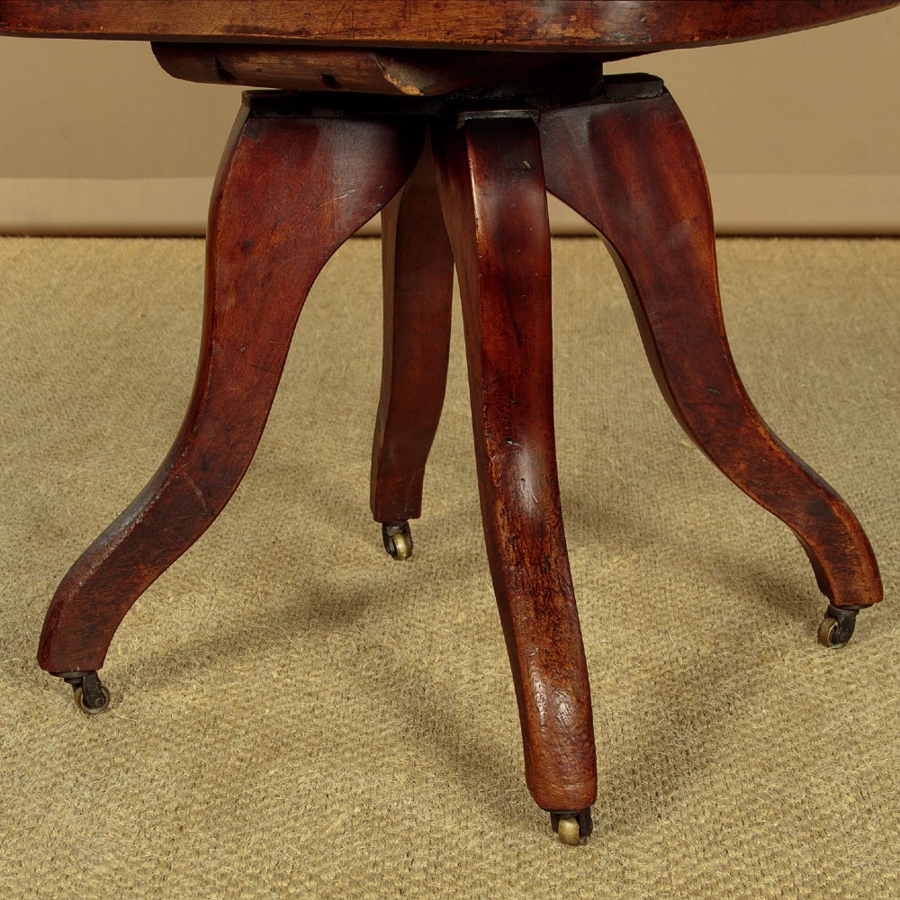 A late Victorian walnut revolving desk chair featuring turned spindles, a curved backrest, a shaped contoured seat, and splayed legs with brass castors. View VIII