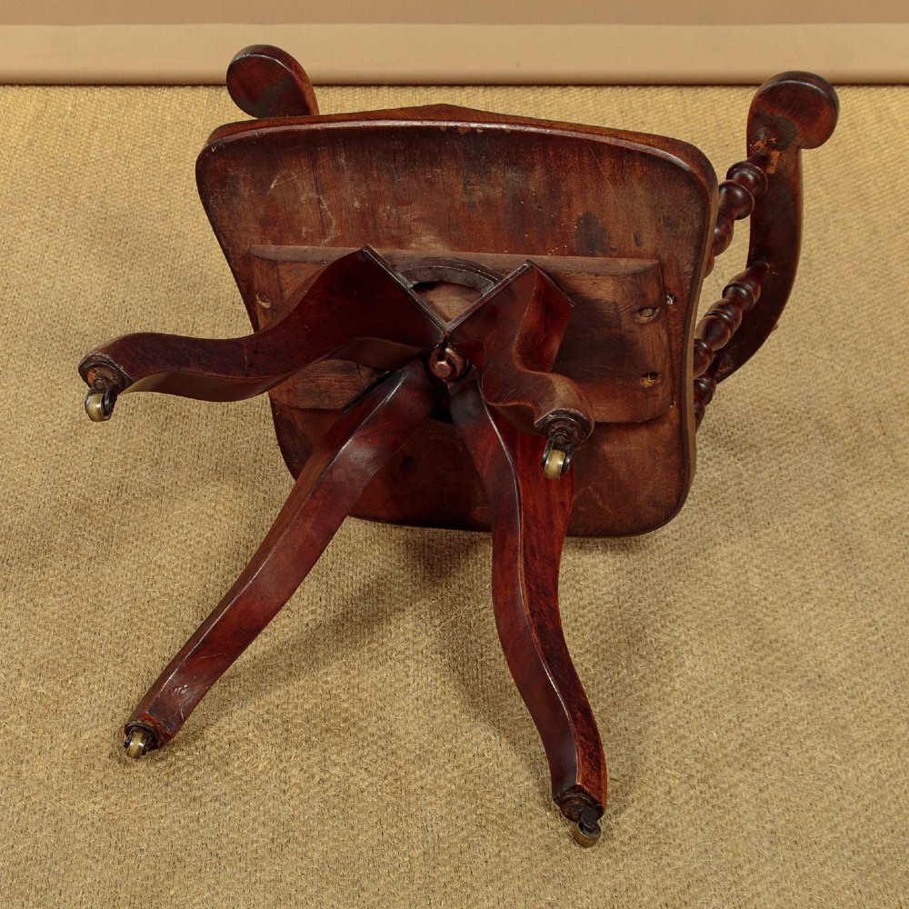 A late Victorian walnut revolving desk chair featuring turned spindles, a curved backrest, a shaped contoured seat, and splayed legs with brass castors. View X