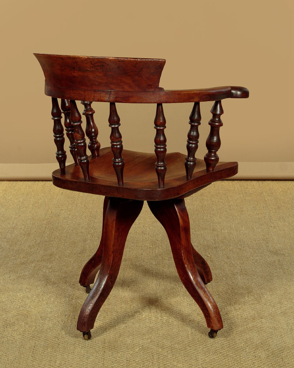 A late Victorian walnut revolving desk chair featuring turned spindles, a curved backrest, a shaped contoured seat, and splayed legs with brass castors. View XI
