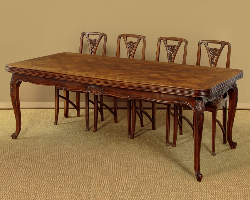 A rectangular French revival walnut dining table featuring a parquetry inlaid top, carved apron, and slender cabriole legs. View II