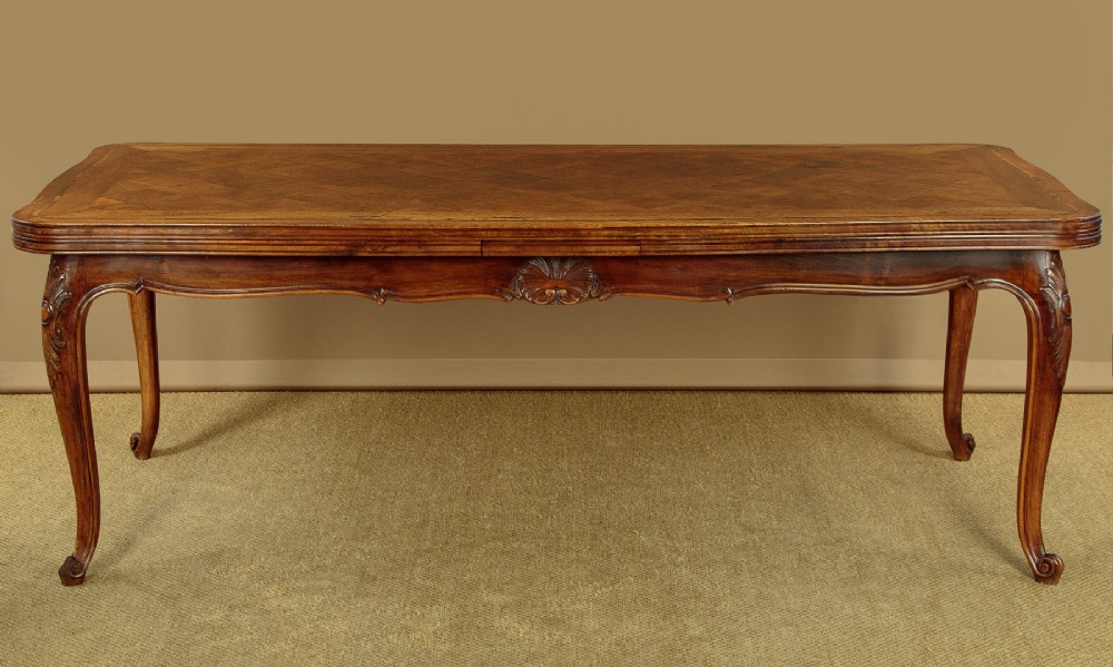 A rectangular French revival walnut dining table featuring a parquetry inlaid top, carved apron, and slender cabriole legs. View III