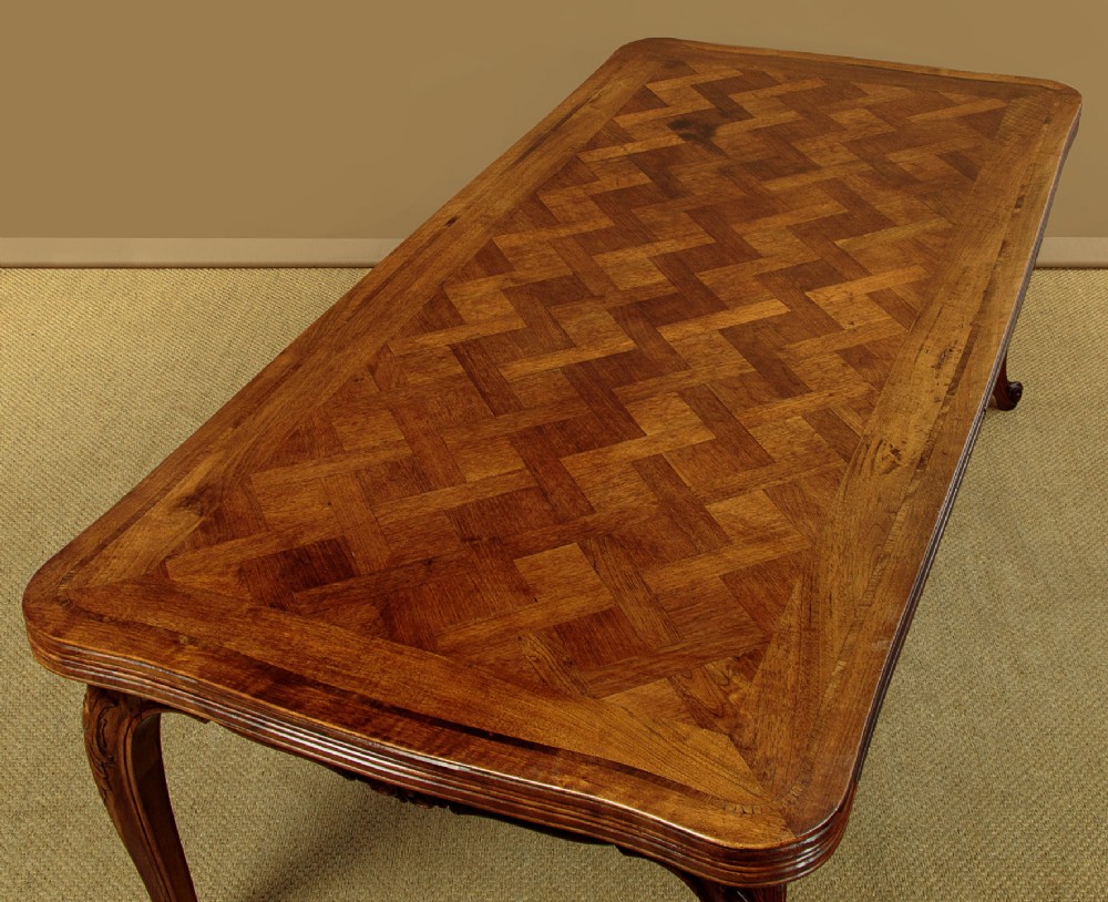 A rectangular French revival walnut dining table featuring a parquetry inlaid top, carved apron, and slender cabriole legs. View IV