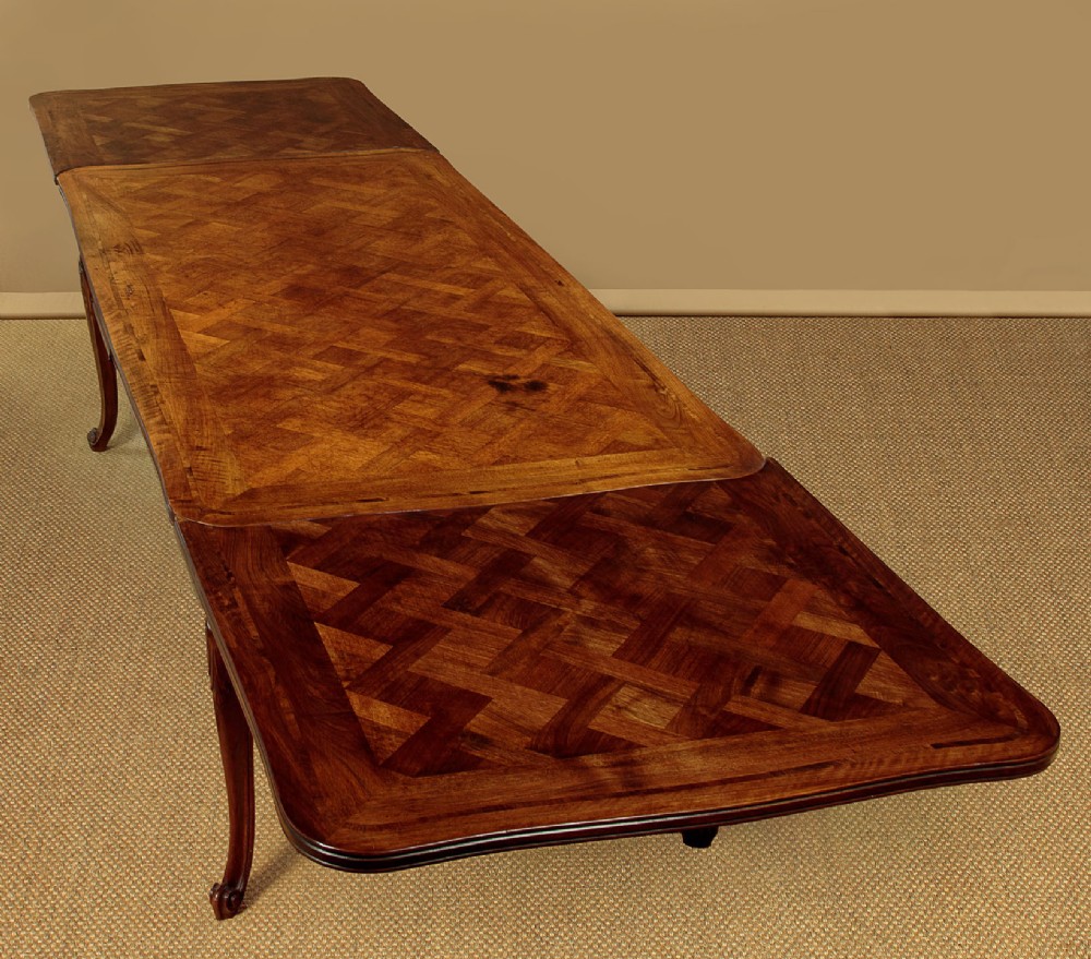 A rectangular French revival walnut dining table featuring a parquetry inlaid top, carved apron, and slender cabriole legs. View VI