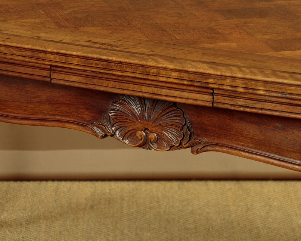 A rectangular French revival walnut dining table featuring a parquetry inlaid top, carved apron, and slender cabriole legs. View VIII