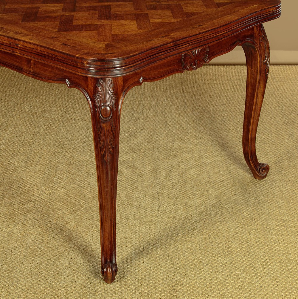 A rectangular French revival walnut dining table featuring a parquetry inlaid top, carved apron, and slender cabriole legs. View IX