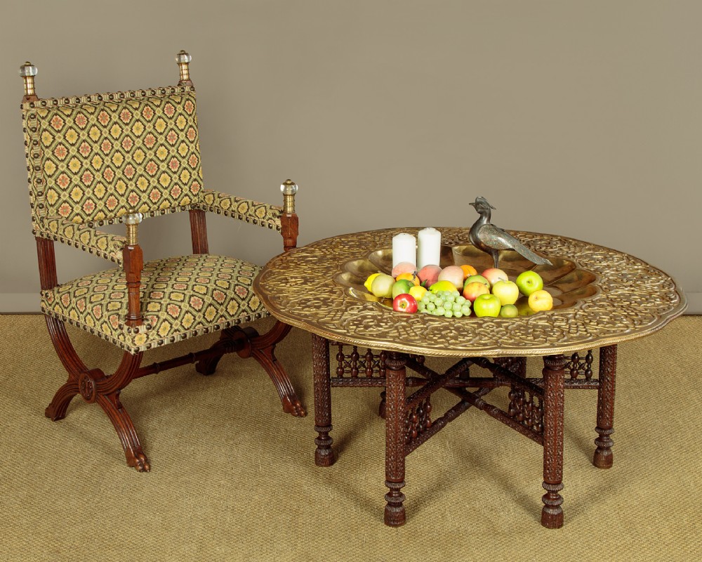 A large round brass tray table featuring detailed floral engravings supported on a dark carved hardwood base with turned legs. View II
