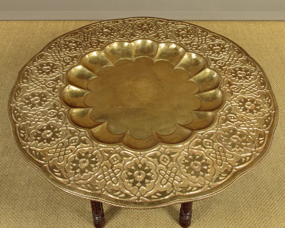 A large round brass tray table featuring detailed floral engravings supported on a dark carved hardwood base with turned legs. View III