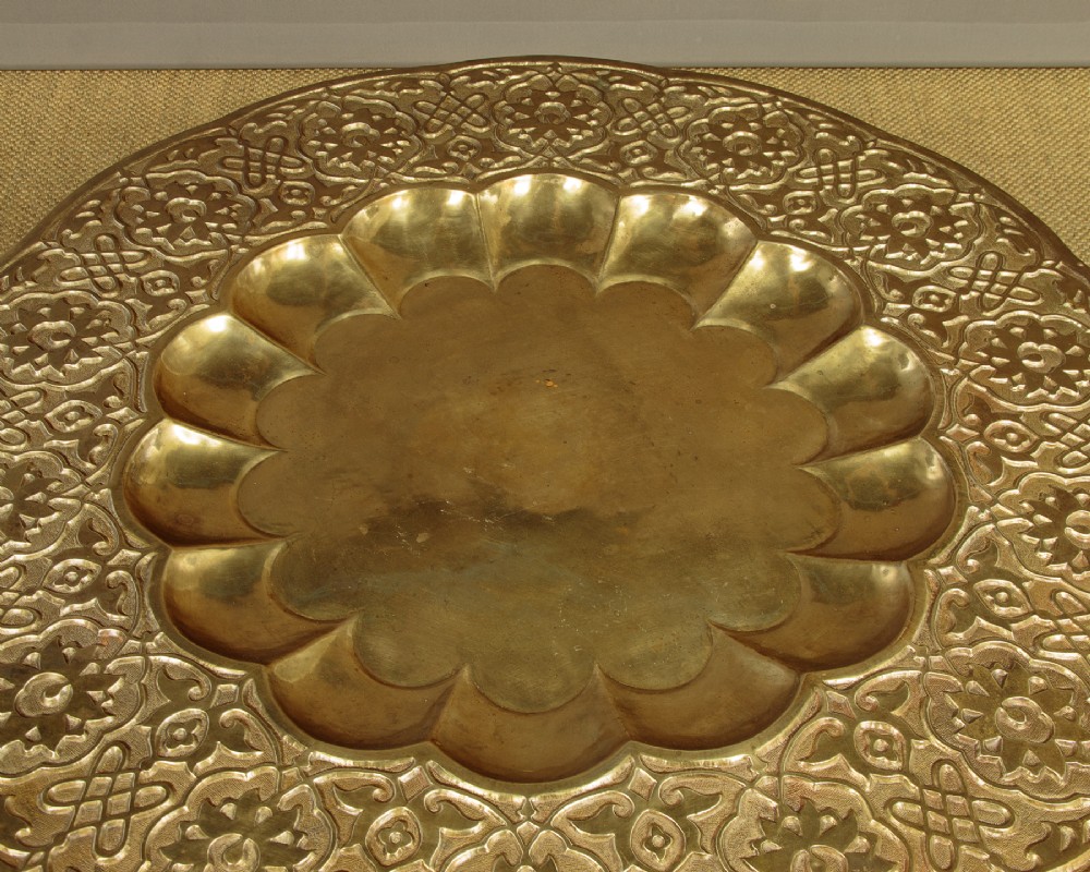 A large round brass tray table featuring detailed floral engravings supported on a dark carved hardwood base with turned legs. View IV