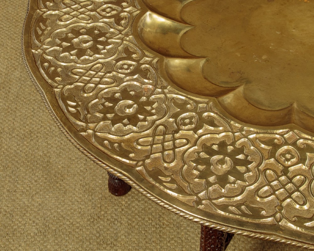 A large round brass tray table featuring detailed floral engravings supported on a dark carved hardwood base with turned legs. View V
