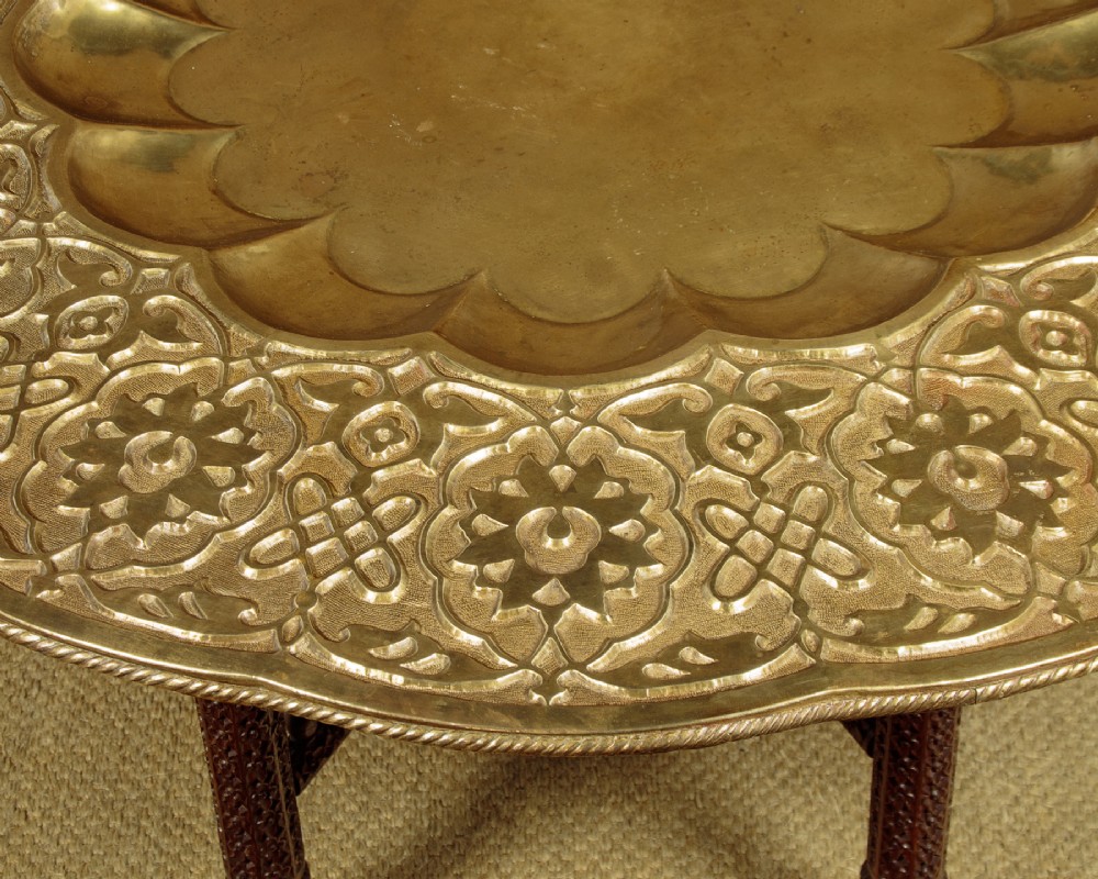 A large round brass tray table featuring detailed floral engravings supported on a dark carved hardwood base with turned legs. View VI