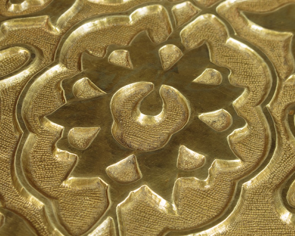 A large round brass tray table featuring detailed floral engravings supported on a dark carved hardwood base with turned legs. View VII