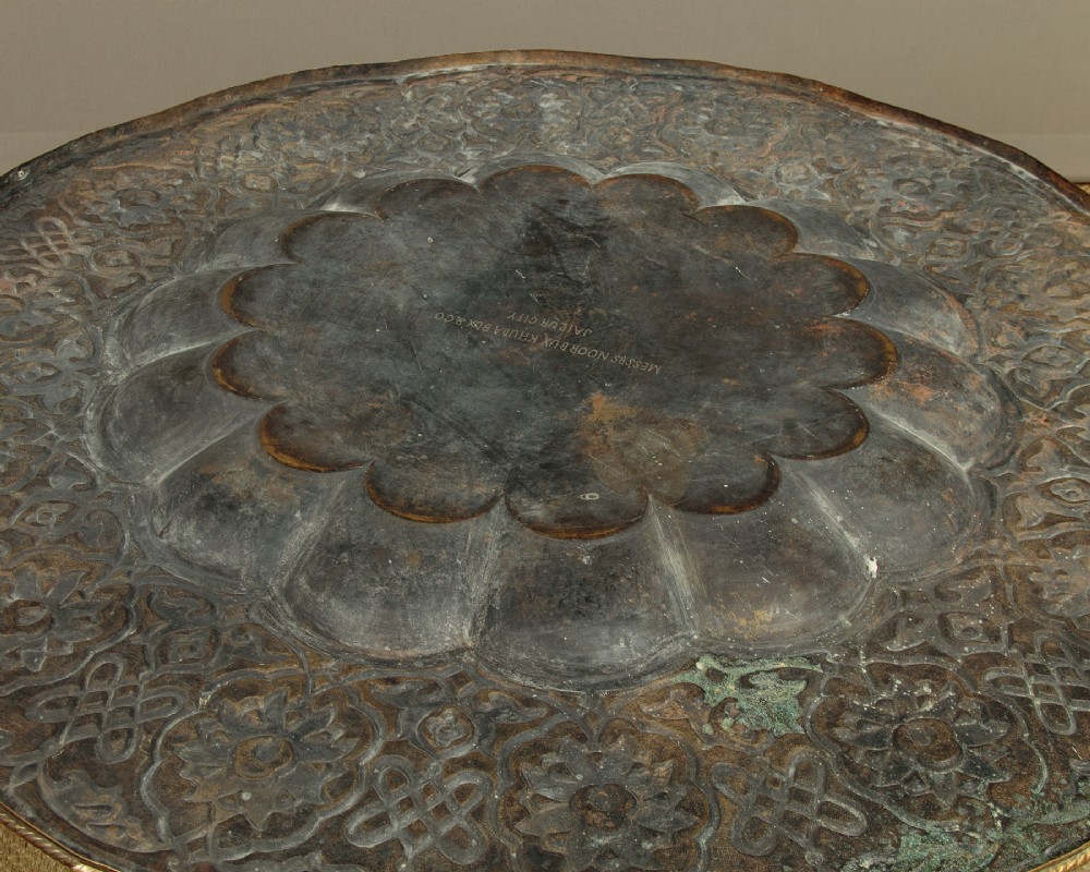 A large round brass tray table featuring detailed floral engravings supported on a dark carved hardwood base with turned legs. View X