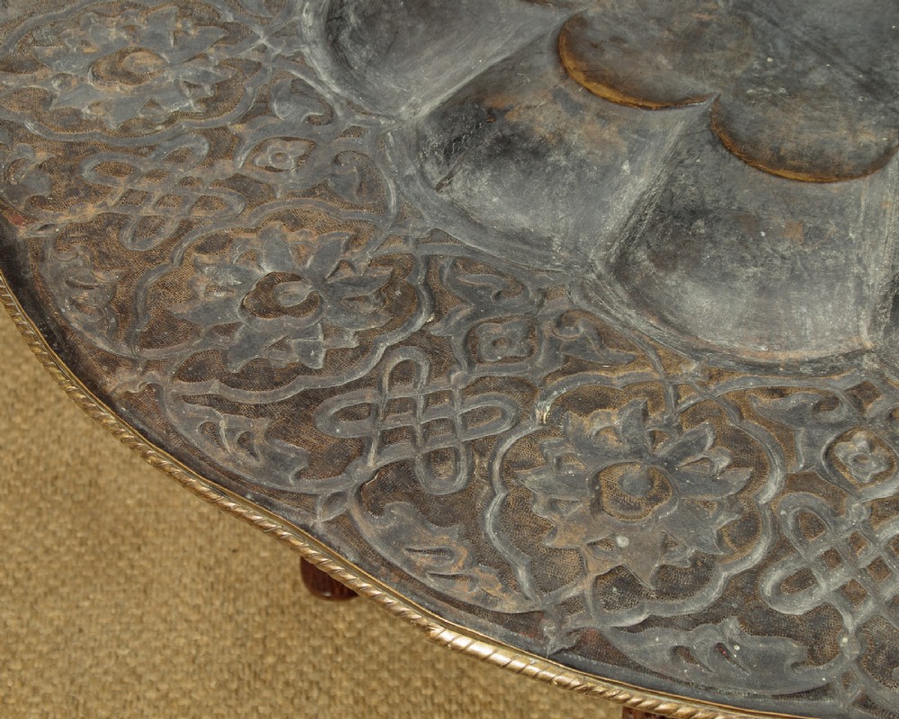 A large round brass tray table featuring detailed floral engravings supported on a dark carved hardwood base with turned legs. View XI
